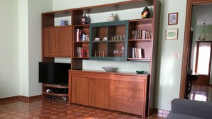 A living room with a TV, wooden cabinets, and shelves with books and decorative items.