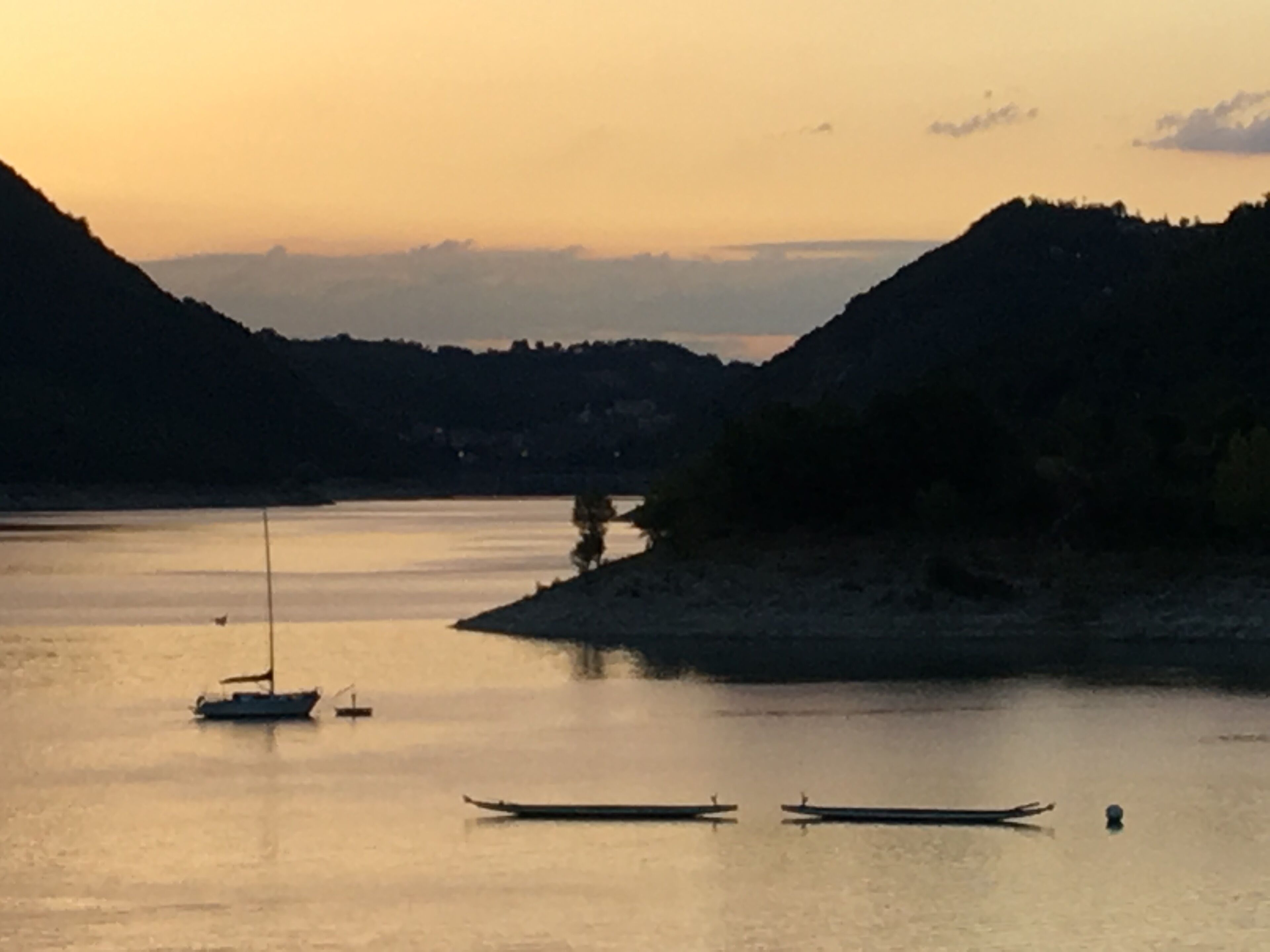 A calm river with boats and a hilly landscape in the background.