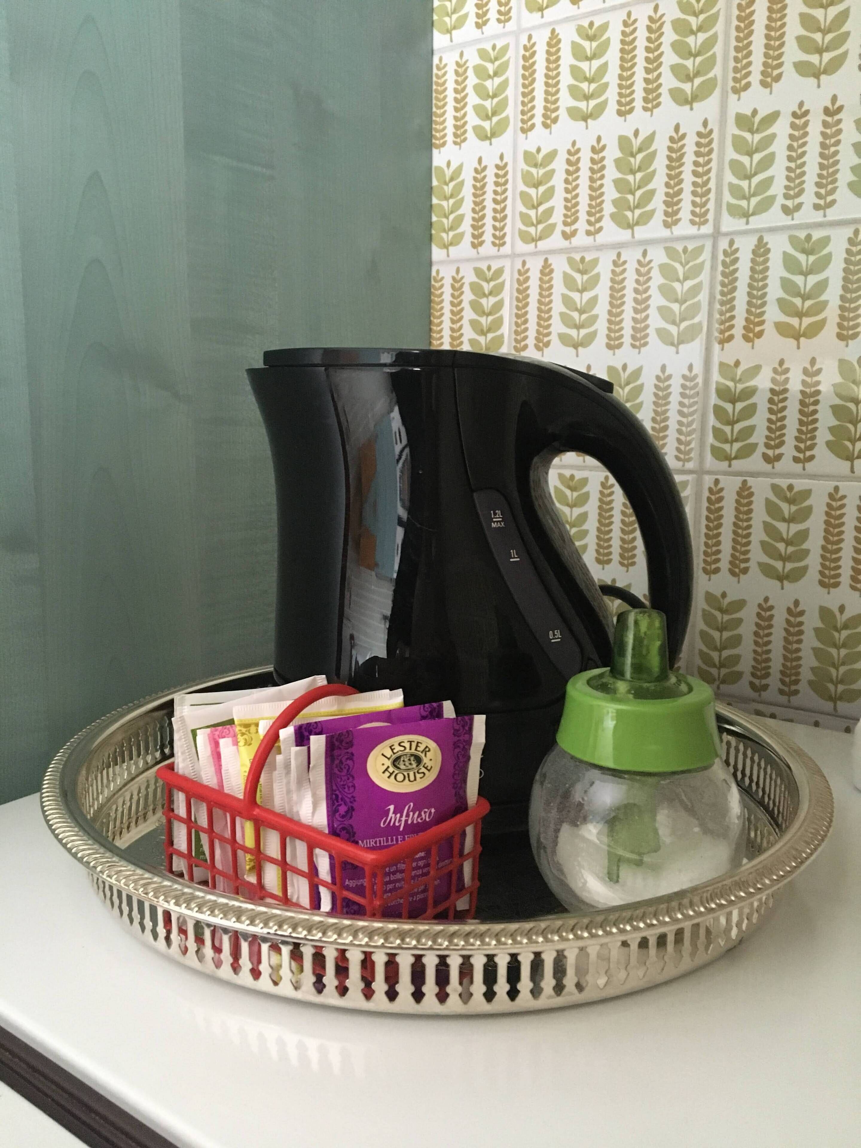 A kitchen counter with a black coffee maker, a red basket with tea bags, and a green water bottle.