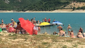 A beach with people sunbathing and swimming, a red tent, and a dock.