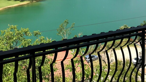 A view of a lake surrounded by hills, with a balcony railing in the foreground.