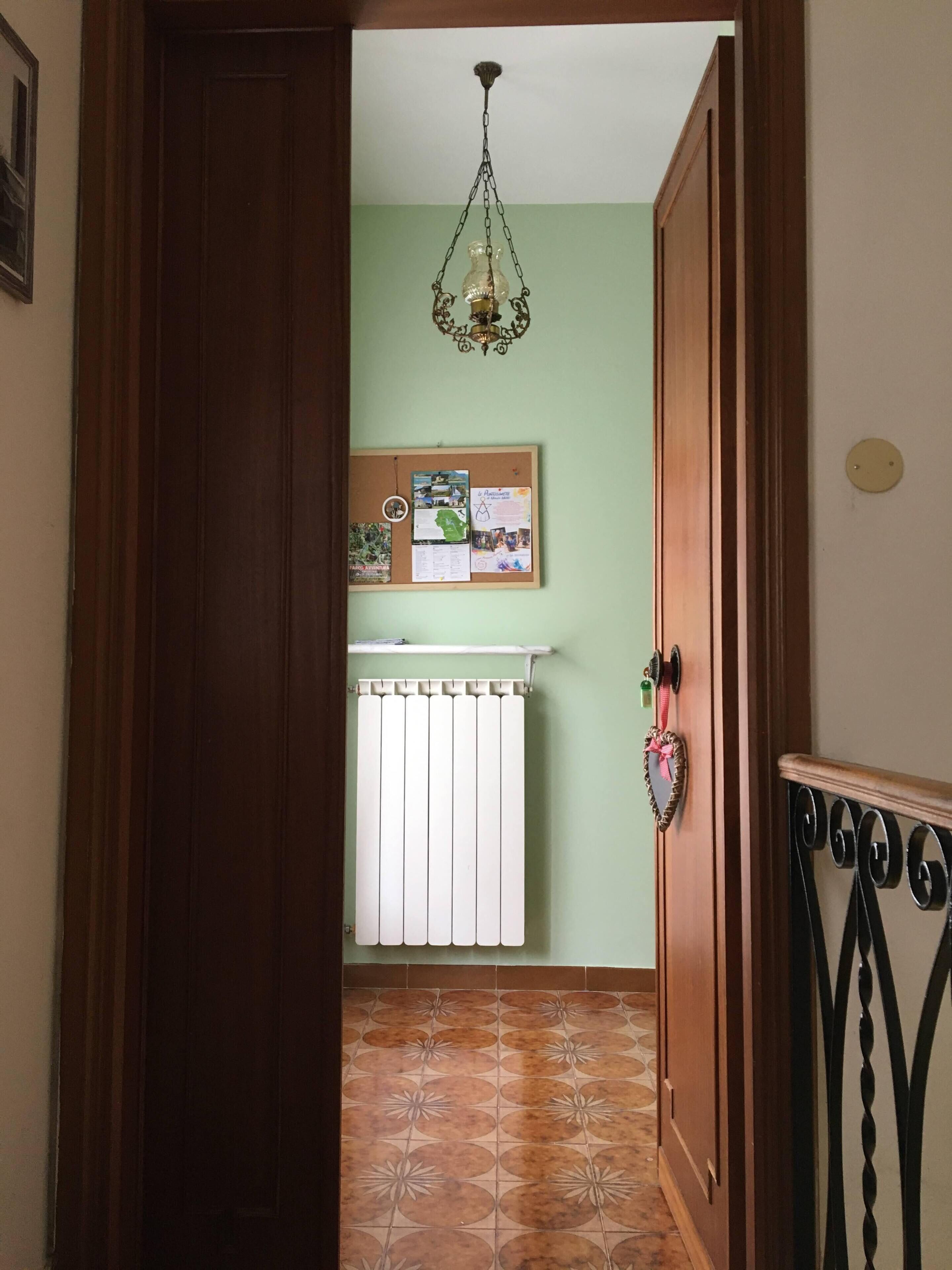A hallway with a radiator, a corkboard with papers, and a patterned floor.