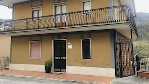 A two-story building with a balcony, a door, and a small garden area.