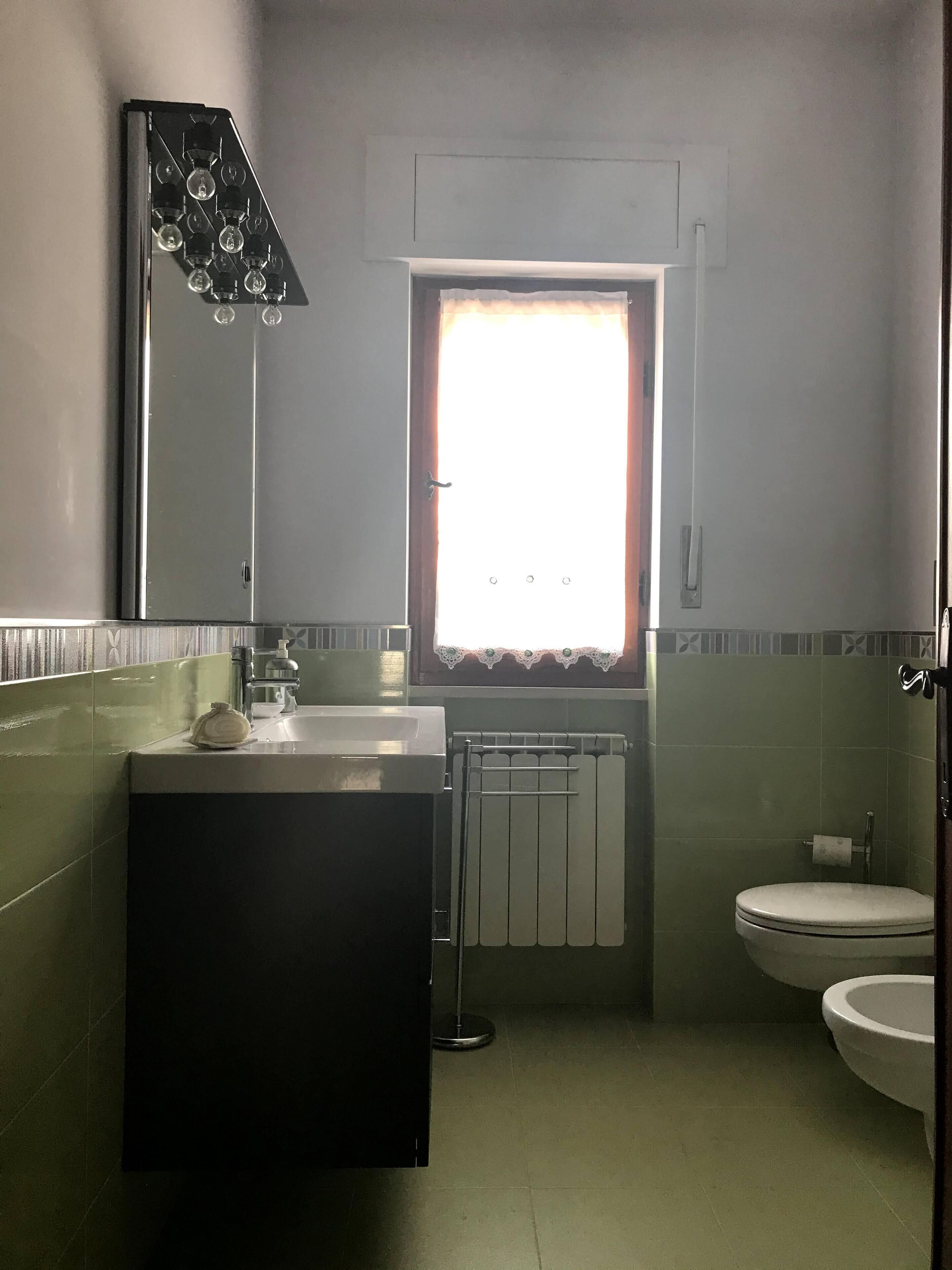 Une salle de bain équipée d’un lavabo, d’un miroir, de toilettes et d’une fenêtre avec des rideaux.