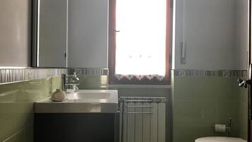 Une salle de bain équipée d’un lavabo, d’un miroir, de toilettes et d’une fenêtre avec des rideaux.