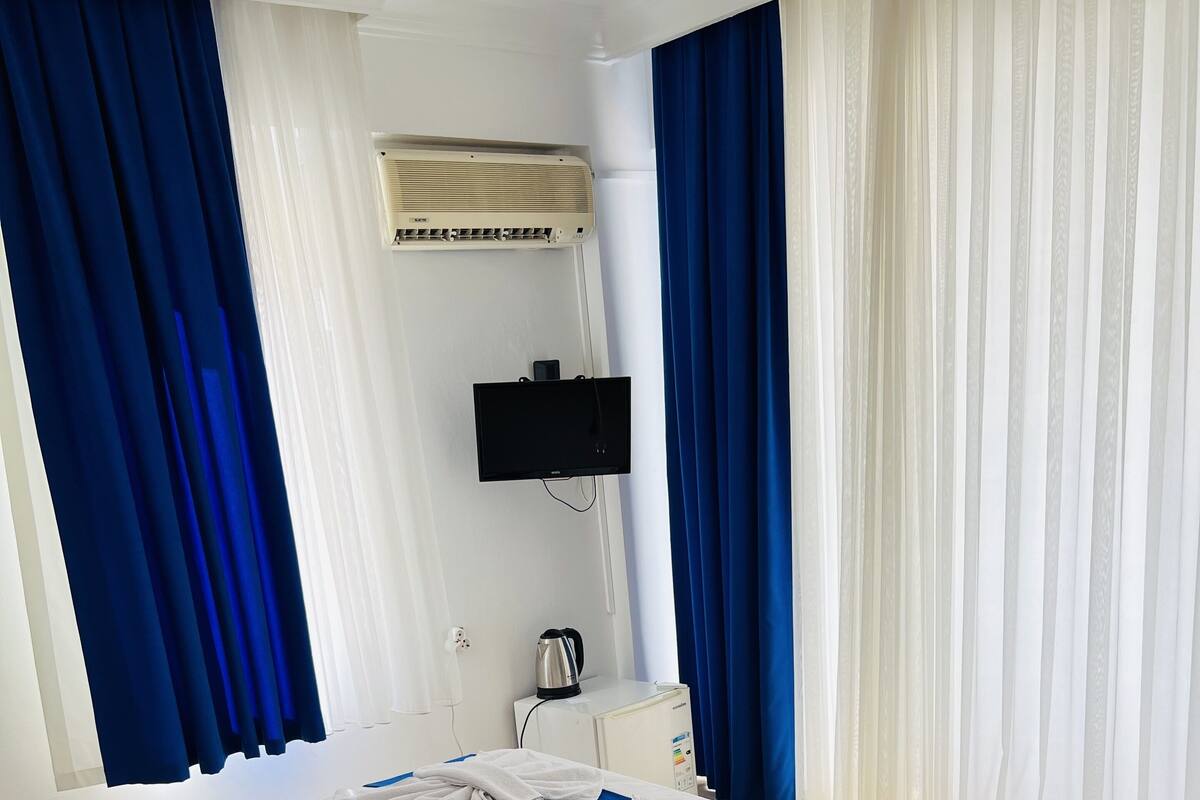 A hotel room with a bed, a TV mounted on the wall, a kettle, and a remote control on a side table.