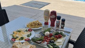 A dining table with a variety of food items including eggs, bread, and vegetables, set against a poolside view.
