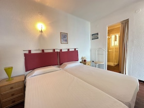 Hotelkamer met een bed, nachtkastje, lamp, foto aan de muur en een zichtbare badkamer door een open deur.