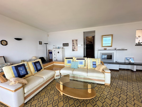 A living room with a sofa, a glass coffee table, patterned carpet, and a fireplace. - Agi Villa Poncella Casa for rent in Roses Girona. (Roses)