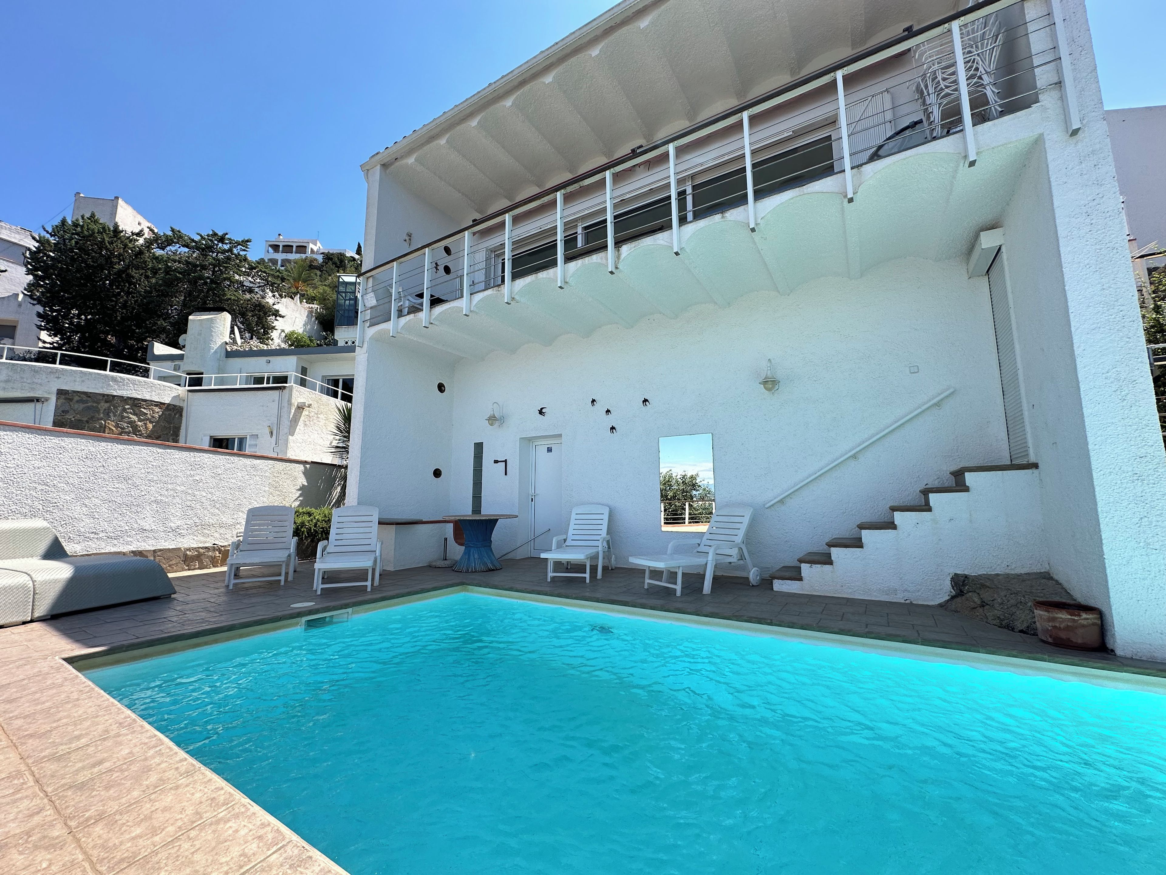 Ein Swimmingpool mit weißen Liegestühlen, einer Treppe und einem Gebäude mit Balkonen.