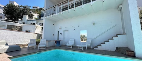 Ein Swimmingpool mit weißen Liegestühlen, einer Treppe und einem Gebäude mit Balkonen.