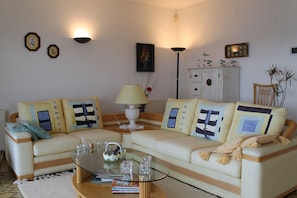 A living room with two cream-colored sofas, a glass coffee table, and a white cabinet.