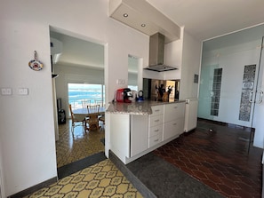 Een moderne keuken met uitzicht op de oceaan, een eethoek met tafel en stoelen, en een gang naar een glazen deur.