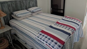 A bedroom with a bed, a bedside table, a lamp, a window with blinds, a wall clock, and a door with a sliding mechanism.