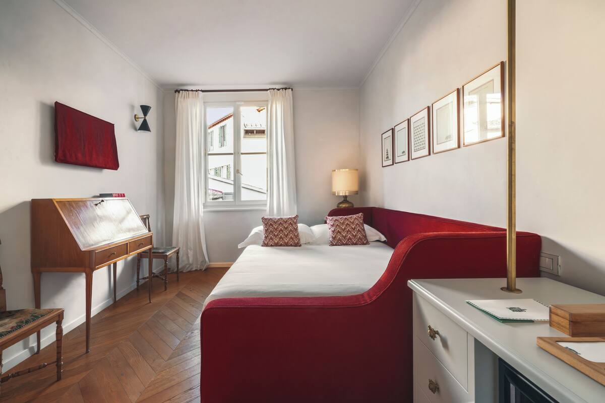 A bedroom with a bed, a desk, a chair, a lamp, and a window with curtains.