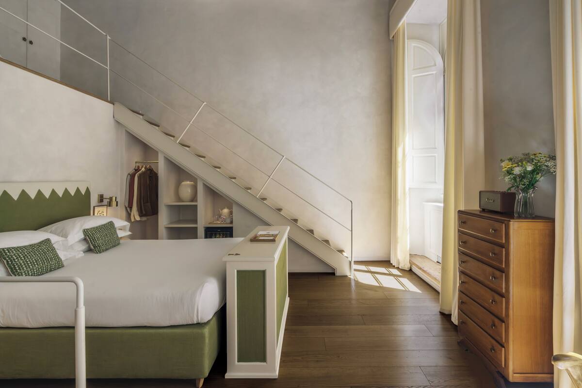 A bedroom with a bed, a dresser, a nightstand, a staircase, and a window with curtains.