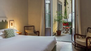 Une chambre d’hôtel avec un lit, deux chaises, une plante en pot et une vue sur le balcon extérieur.