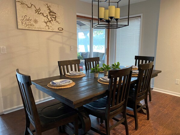A dining room with a wooden table and chairs, a map on the wall, and a window with blinds.