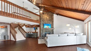 Un vaste espace de vie agrémenté d’une cheminée en pierre, d’un canapé blanc et d’un escalier en bois.
