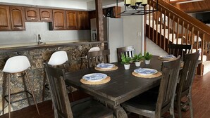 Un coin repas avec une table en bois dressée pour quatre personnes, entourée de chaises, dans une cuisine dotée de meubles en bois et d’un pare-feu en pierre.