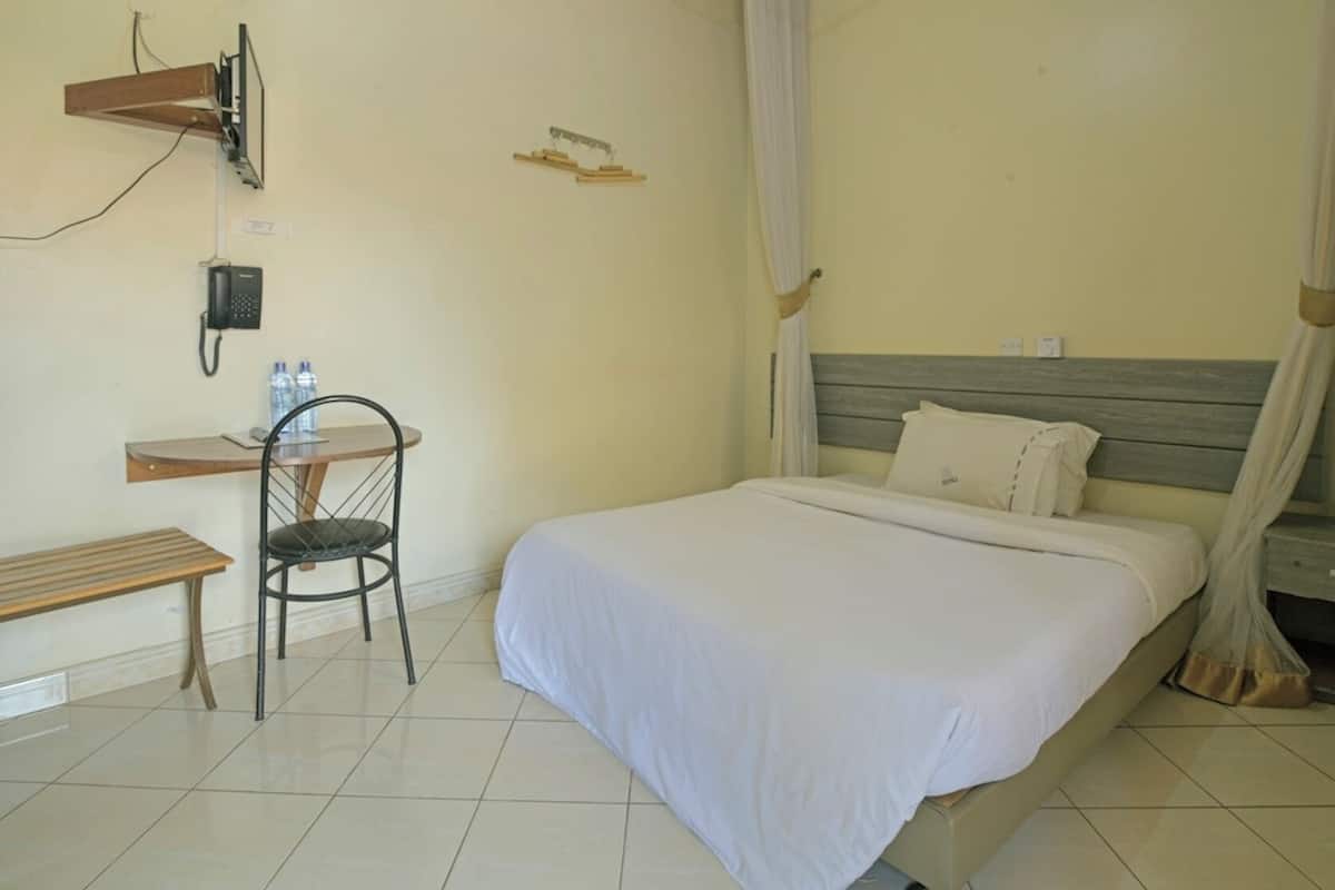 A hotel room with a bed, a desk with a chair, a telephone, and a wall-mounted fan.