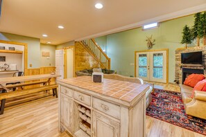 A spacious living room with a wooden staircase, a fireplace, and a dining area with a bench and table.