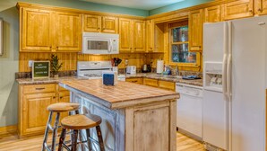 A kitchen with wooden cabinets, a white refrigerator, a microwave, a toaster, and a sink. There are two stools at the island.