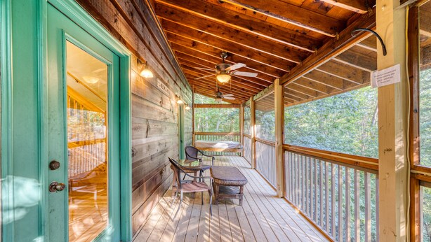 A wooden deck with a ceiling fan, a table with chairs, and a view of trees.
