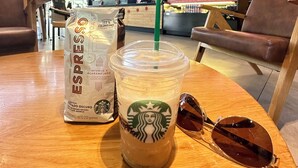 Un vaso de Starbucks con una pajita y gafas de sol sobre una mesa de madera en una cafetería con sillas de cuero.
