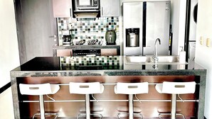 Una cocina moderna con una isla central, taburetes de bar, un microondas, un refrigerador y un salpicadero de azulejos.