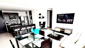 Una sala de estar moderna con comedor, cocina y televisor mostrando una película.