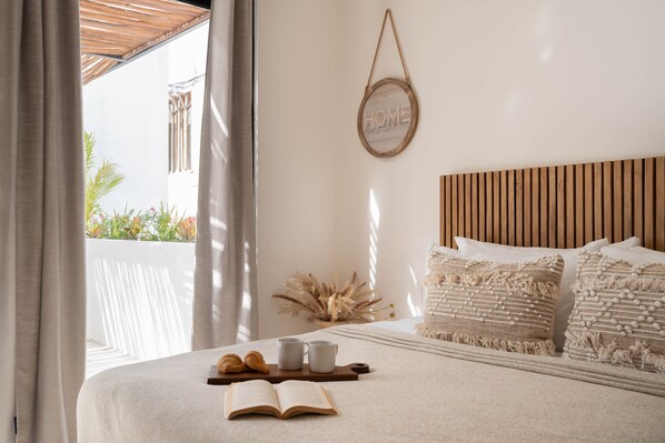 A neatly made bed with a book, two cups, and a croissant, a wooden headboard, and a wall-mounted sign that reads "HOME".
