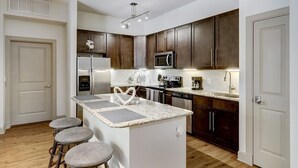 A modern kitchen with dark wood cabinets, stainless steel appliances, and a granite countertop. - Stylish 2 BR in the Med Center near NRG Stadium (Houston)