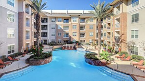 A swimming pool surrounded by lounge chairs and palm trees, with a multi-story building in the background. - Stylish 2 BR in the Med Center near NRG Stadium (Houston)