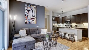 A modern living room with a gray sectional sofa, a coffee table, and a large abstract painting on the wall. - Stylish 2 BR in the Med Center near NRG Stadium (Houston)