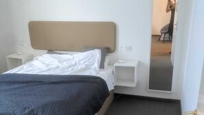 Une chambre à coucher avec un lit, des tables de chevet, un miroir et une porte.