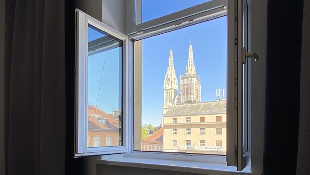 Une chambre d’hôtel dotée d’une grande fenêtre donnant sur un bâtiment historique à deux tours.