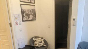 Une petite pièce, peu meublée, avec un bureau et une chaise, une porte donnant sur une autre pièce, et un mur orné de deux tableaux encadrés.
