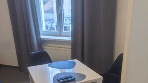Un petit coin repas avec une table blanche et quatre chaises noires. Il y a deux télécommandes sur la table.