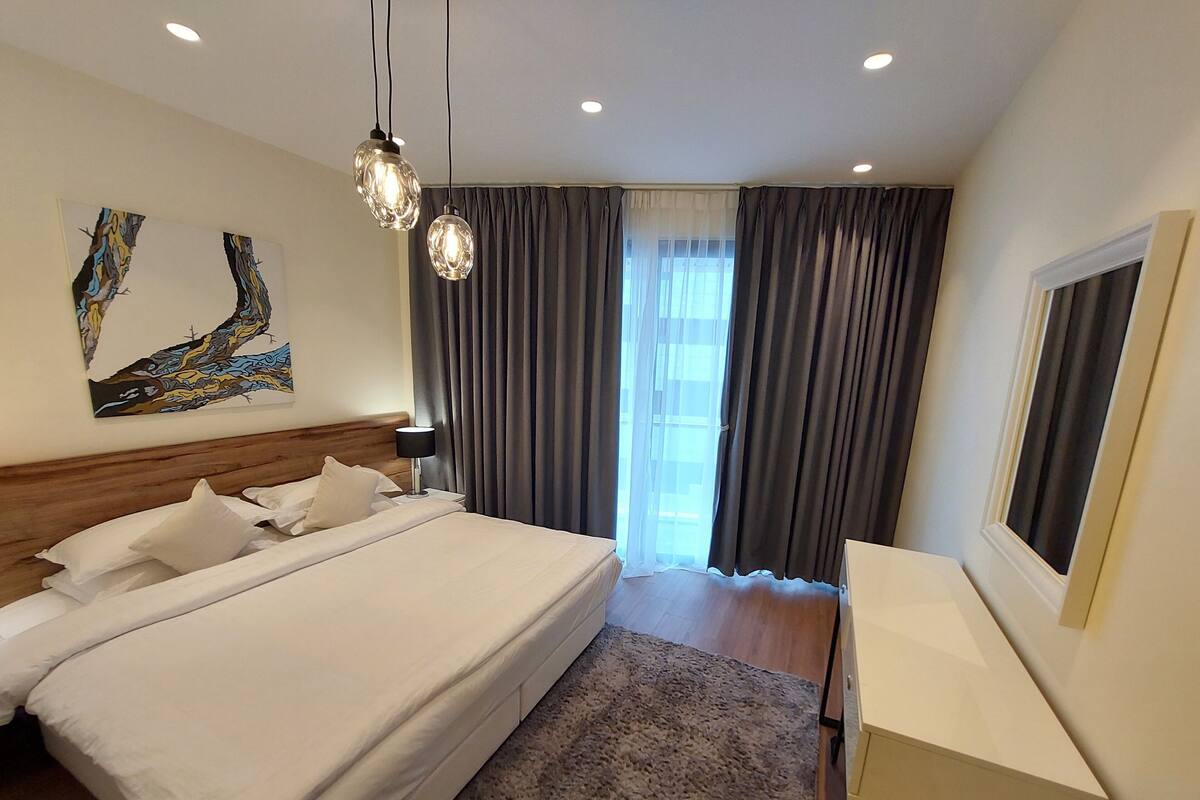 Une chambre d’hôtel moderne dotée d’un grand lit, d’une table de chevet, d’un bureau et d’une grande fenêtre avec des rideaux.
