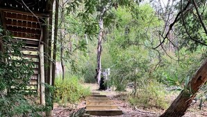Un escalier en bois menant vers le haut, dans une zone boisée où le sol est recouvert de roches et de paillis.