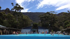 Une piscine entourée de personnes, bordée d’arbres et avec un bâtiment en arrière-plan.