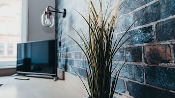 A potted plant in a modern room with a brick wall and a flat-screen TV.