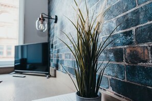 A potted plant in a modern room with a brick wall and a flat-screen TV.