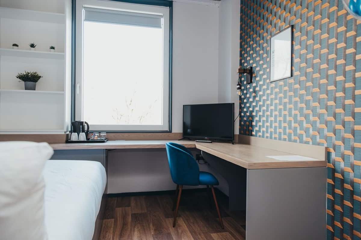 A modern hotel room with a bed, a desk with a chair, a television, and a window.