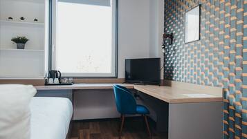 A modern hotel room with a bed, a desk with a chair, a television, and a window.