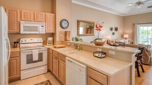 A modern kitchen with wooden cabinets, a microwave, stove, and dishwasher. There is a large island with a sink and a mirror above it. - Way Down in Kokomo (St. Augustine)