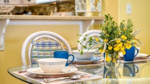 A dining table with a glass top, a vase with yellow flowers, and blue and white cups and saucers. - Mermaid Beach House (St. Augustine)