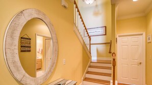 A hallway with a wooden staircase, a large mirror, and a door. - Mermaid Beach House (St. Augustine)