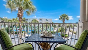 A balcony with a table set for two, overlooking a pool and a street with palm trees and buildings. - Montego Bay (St. Augustine)